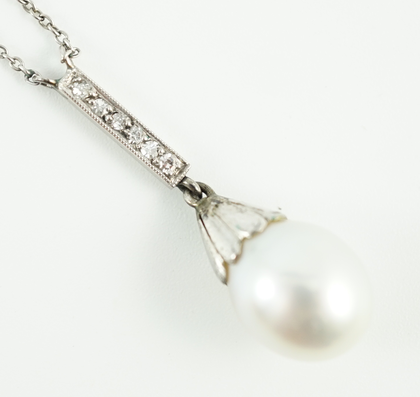 A 1920's platinum, single stone pear shaped cultured pearl and six stone diamond chip set pendant necklace